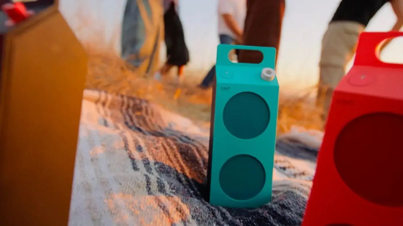 CMF Speaker M in turquoise and orange on a sandy beach at sunset