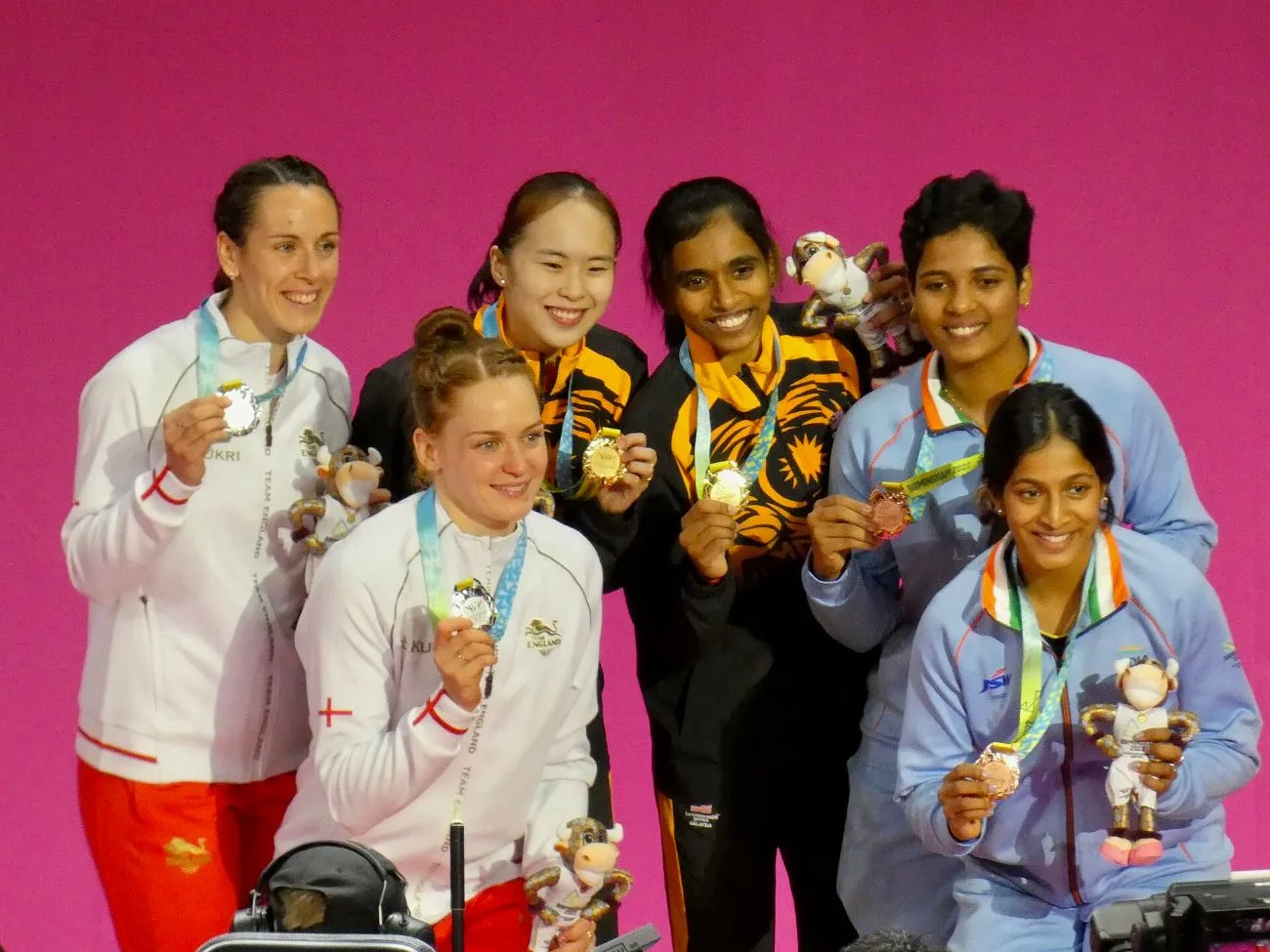 Pearly Tan and M. Thinaah in Malaysia's tiger-stripe kit smiling on the podium with other women's doubles medallists, related to the French Open 2026 final
