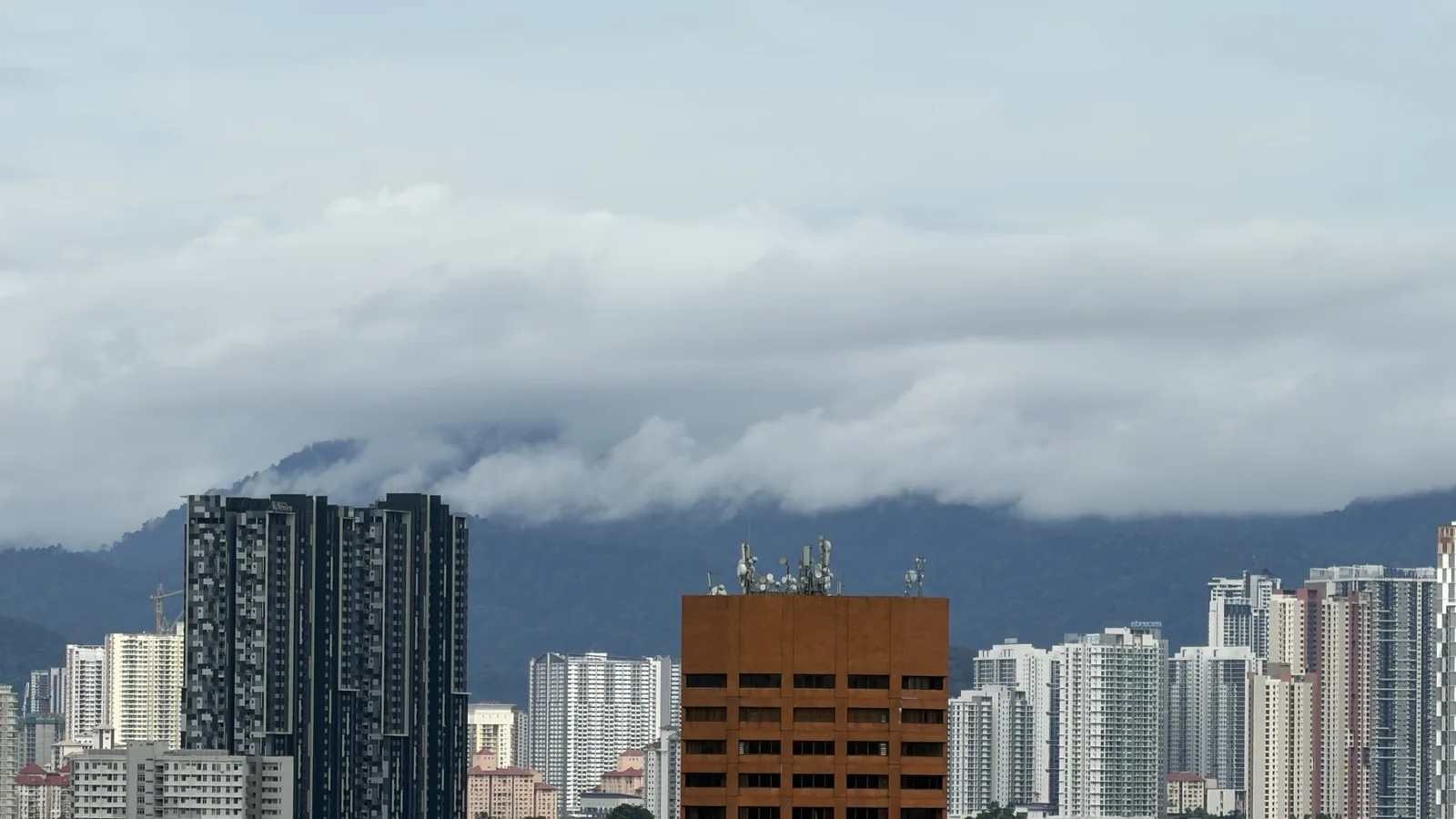 Bangunan-bangunan tinggi Kuala Lumpur dengan awan rendah menyelubungi puncak bukit di belakang