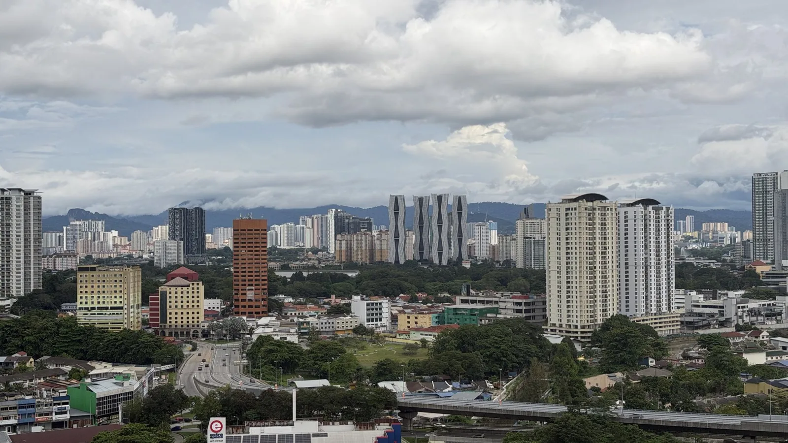 Pemandangan panorama Kuala Lumpur dengan bangunan tinggi, jalan raya dan bukit di kejauhan di bawah langit cerah berawan