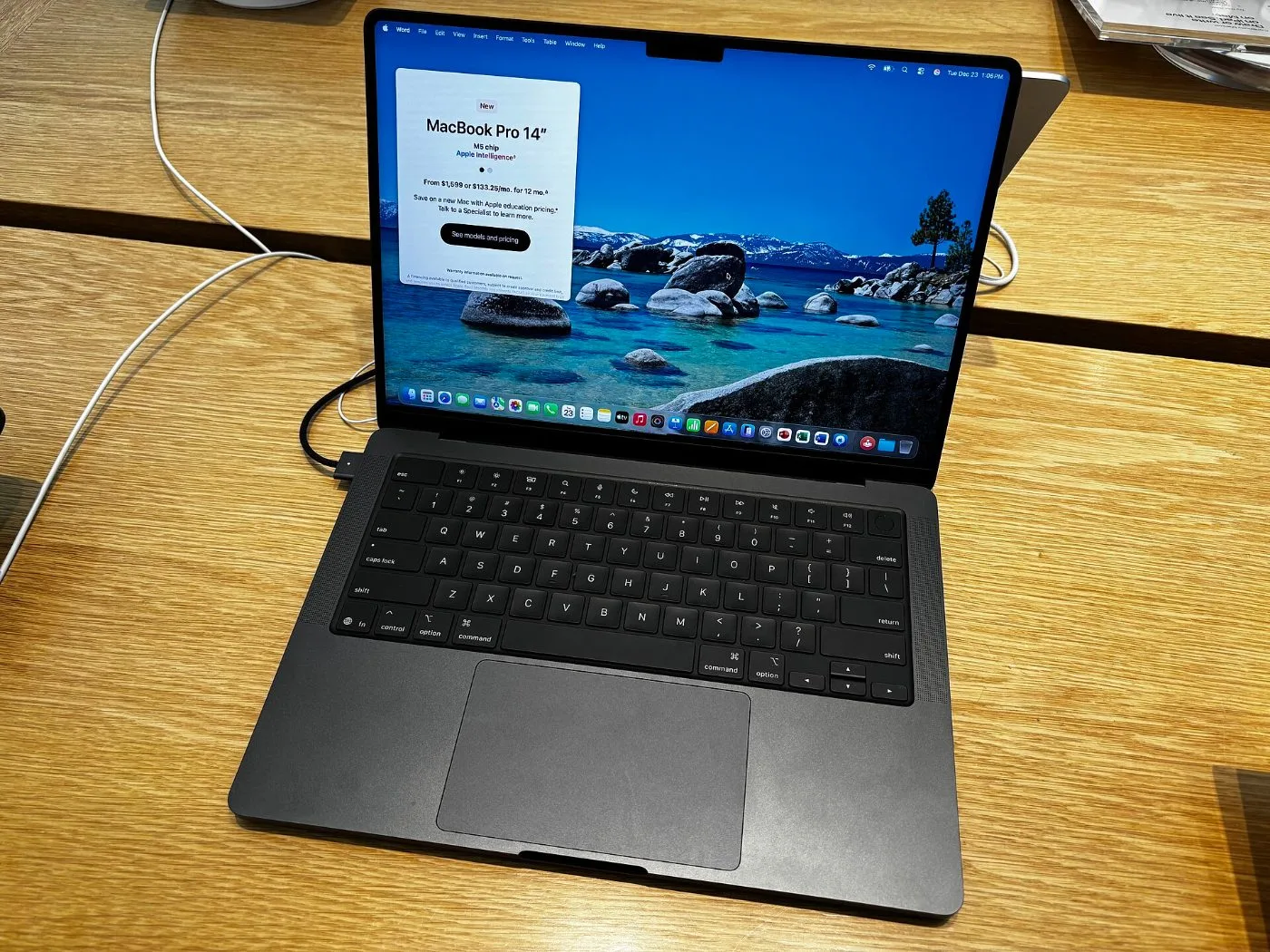 14-дюймовый MacBook Pro на M5 цвета Space Black открыт на деревянном столе, текущая модель перед ожидаемым OLED-MacBook Pro